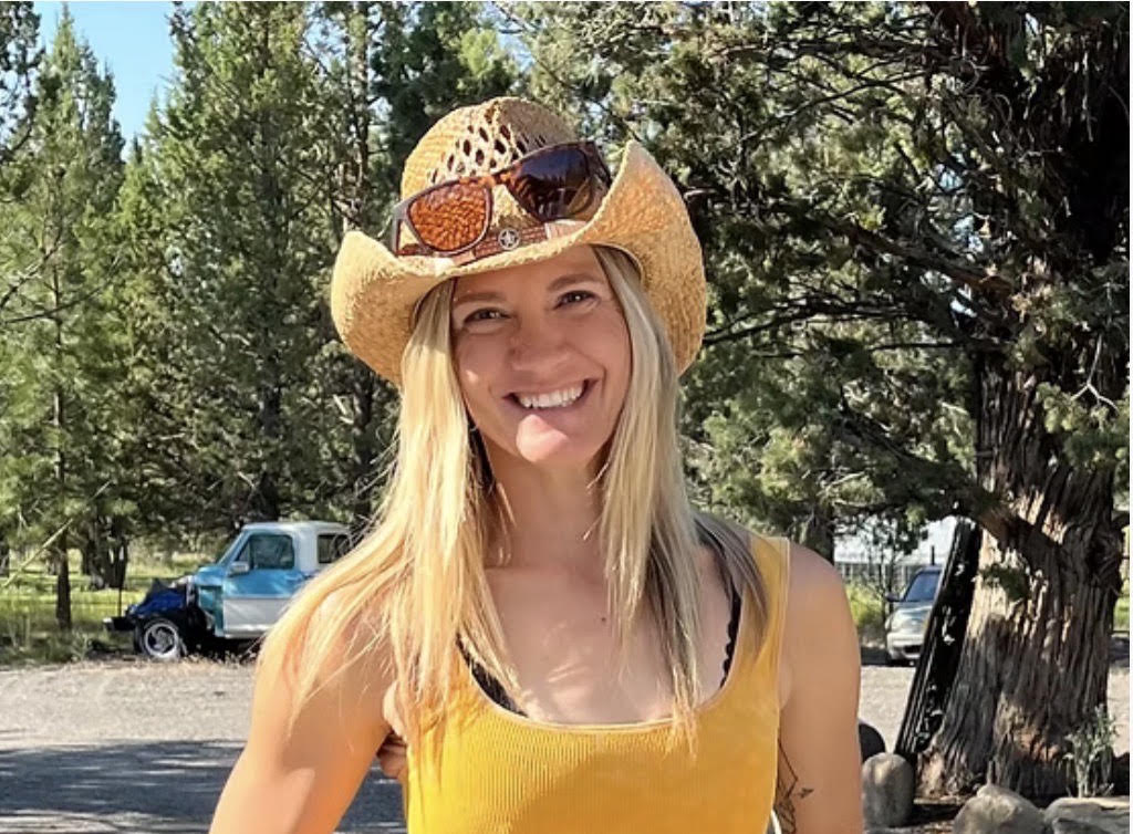 Jamie Bowles smiling outdoors in a straw cowboy hat among Oregon pines